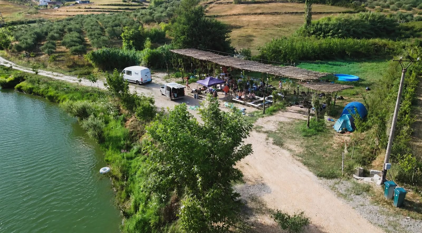 A group under the shaded pergola by the lake, seen from above